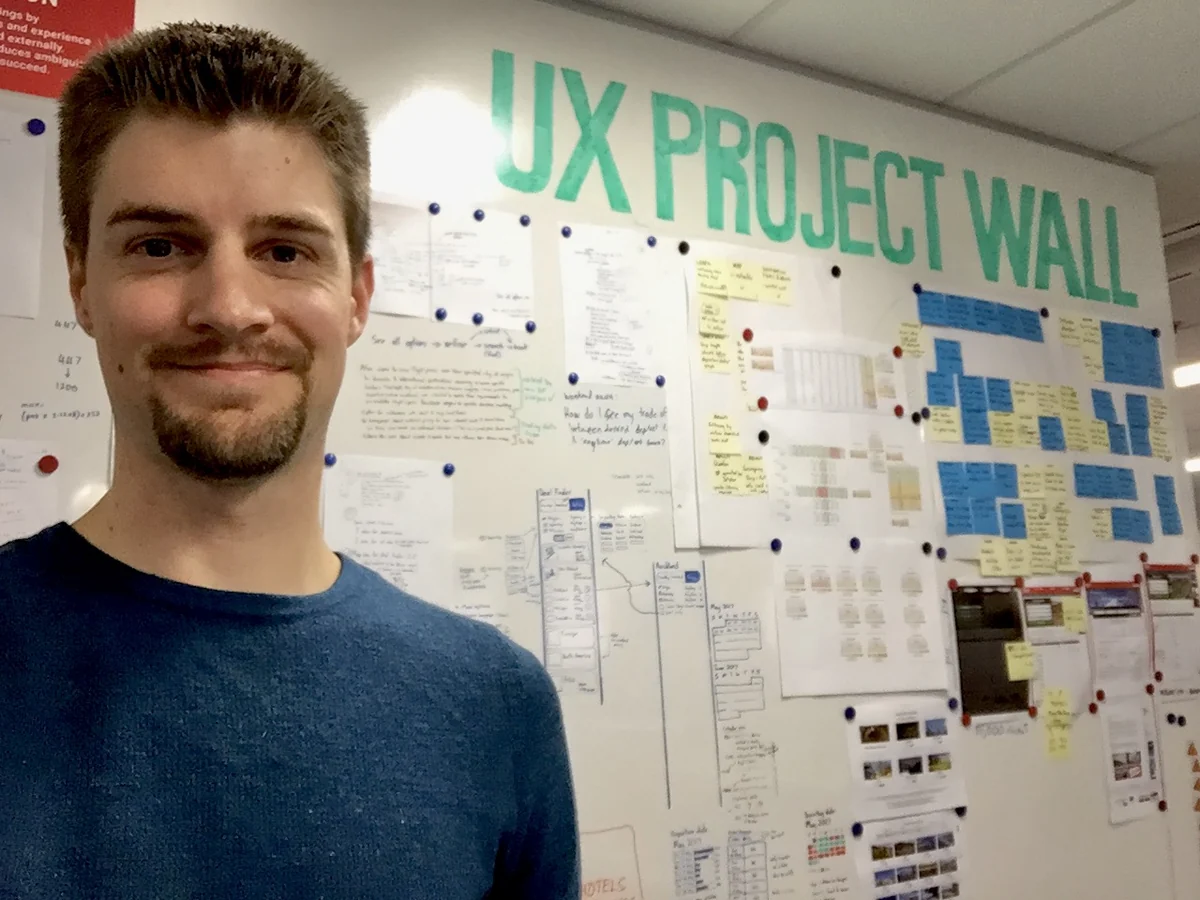 Shannon Murdoch standing in front of the Webjet UX project wall covered in printed screens and annotations.